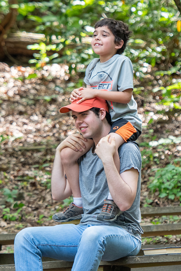Child sits on a family member's shoulders during a Children's Theatre-in-the-woods performance.