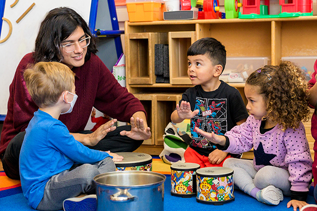 Teacher leads kids in a drumming activity..