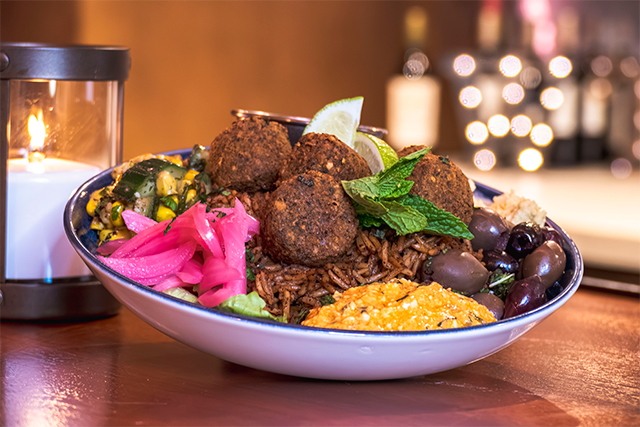 Closeup of a falafel bowl next to a glowing candle.