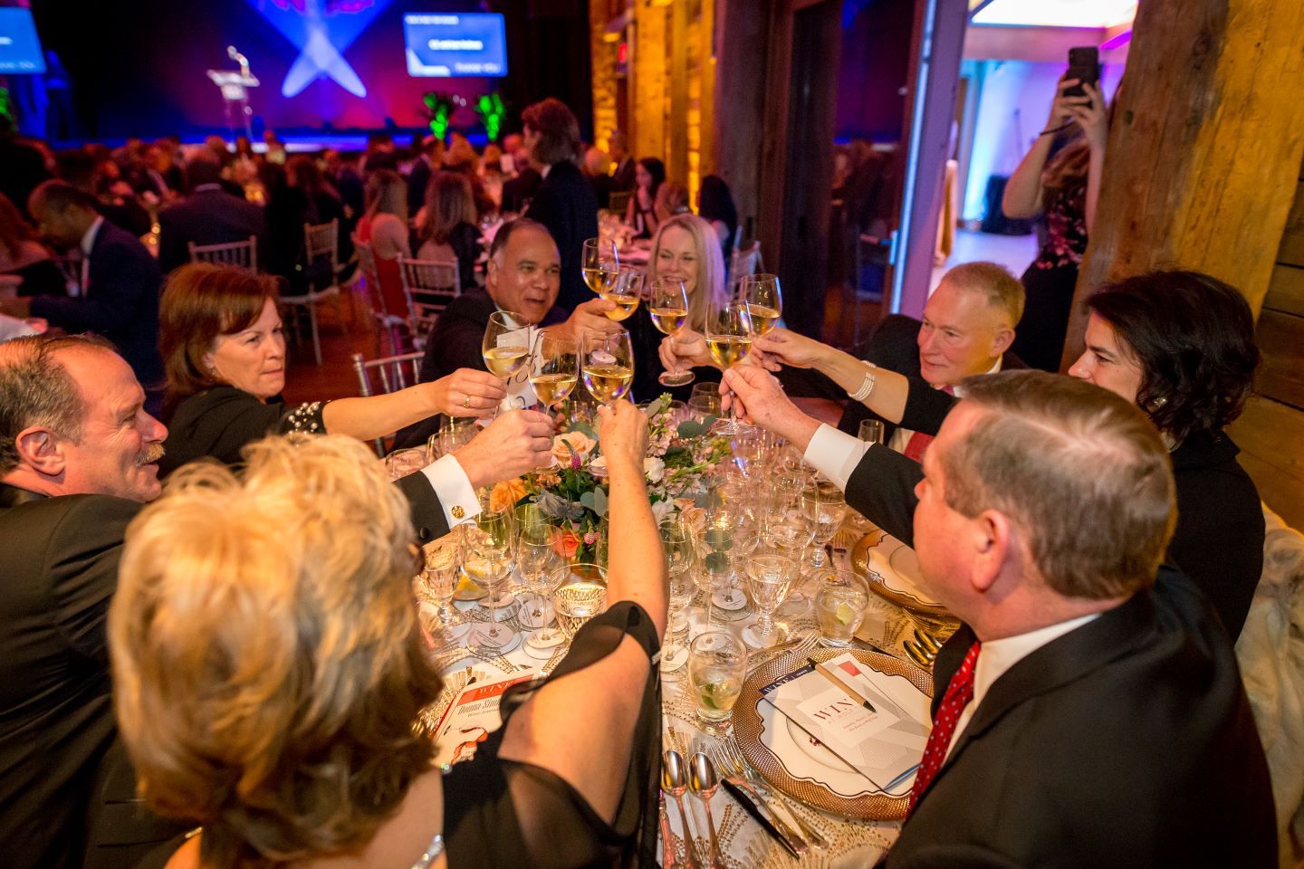 Guests around an elegantly-decorated round table raise their wine glasses in a toast.