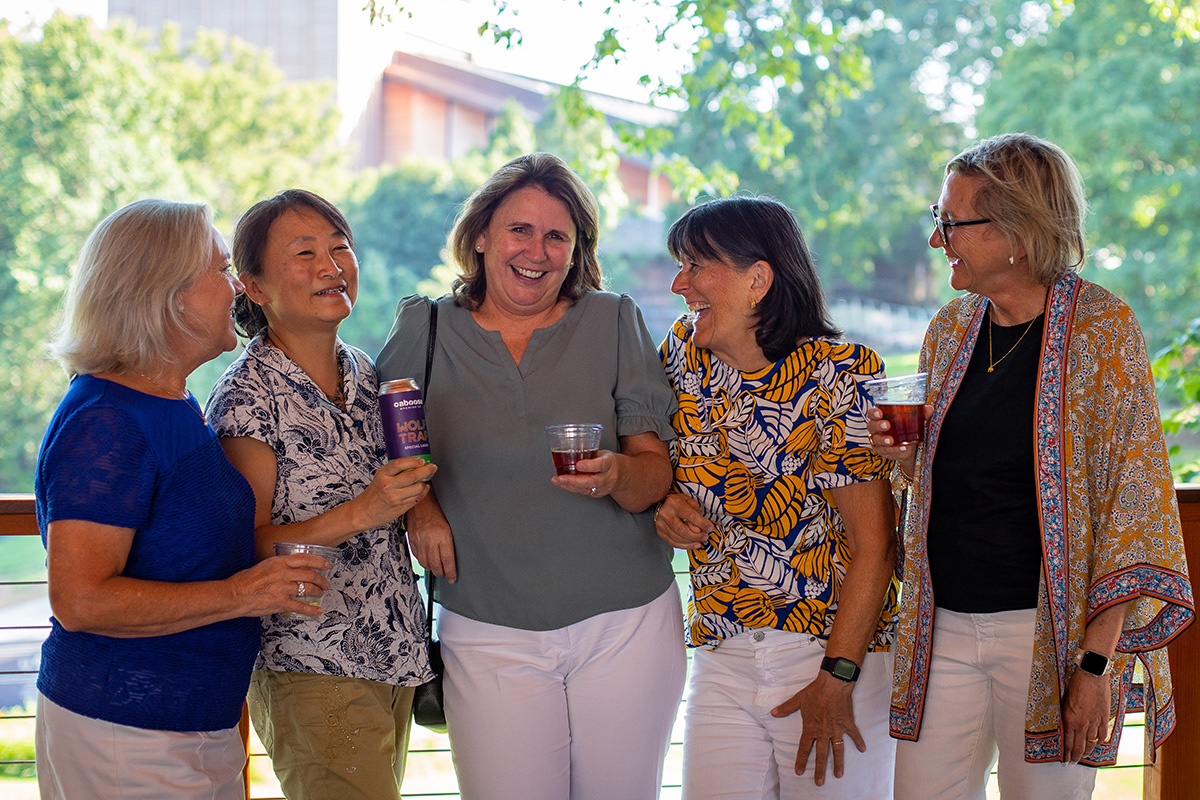 Five women smile and raise wine glasses with the Filene Center in the background.