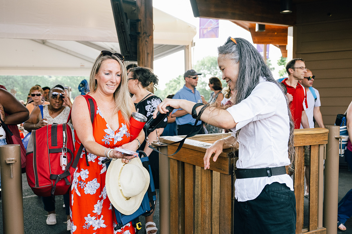 A woman in a red dress has her ticket scanned by a smiling park volunteer.