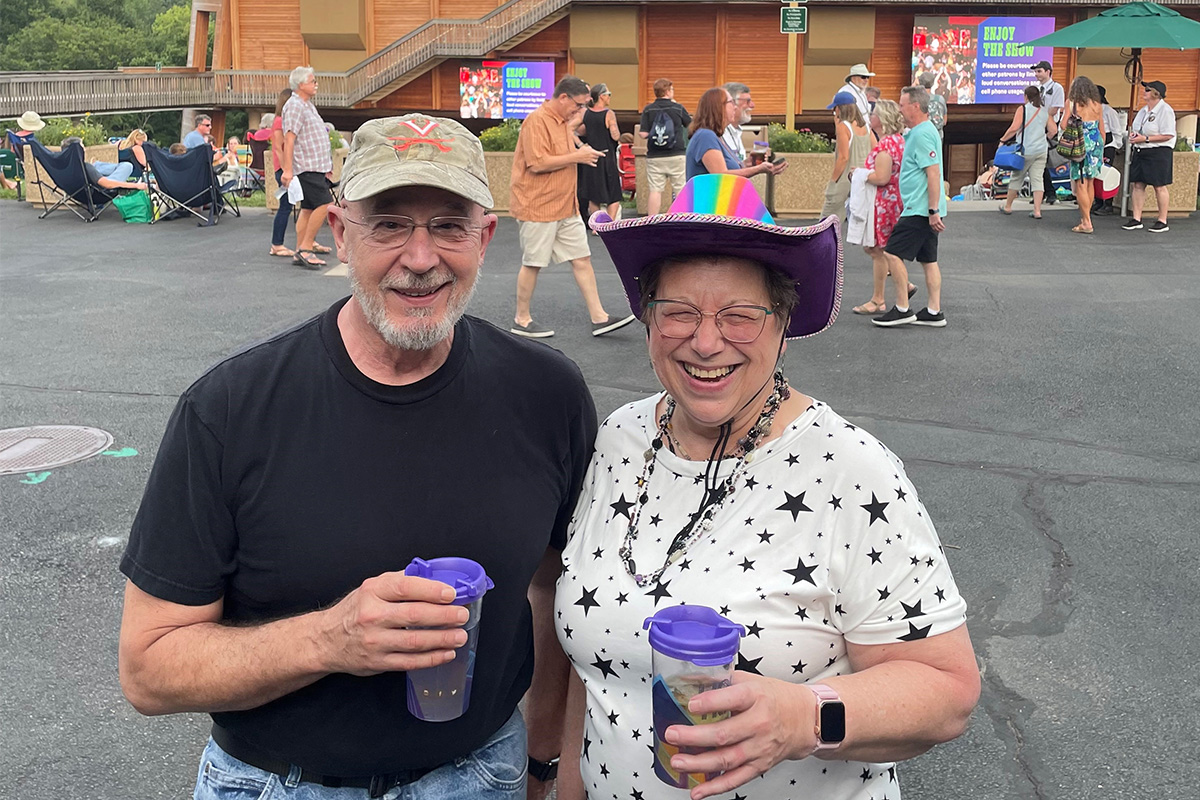 Wolf Trap Volunteer Chris Temple, wearing a colorful cowboy hat, in front of the Filene Center.