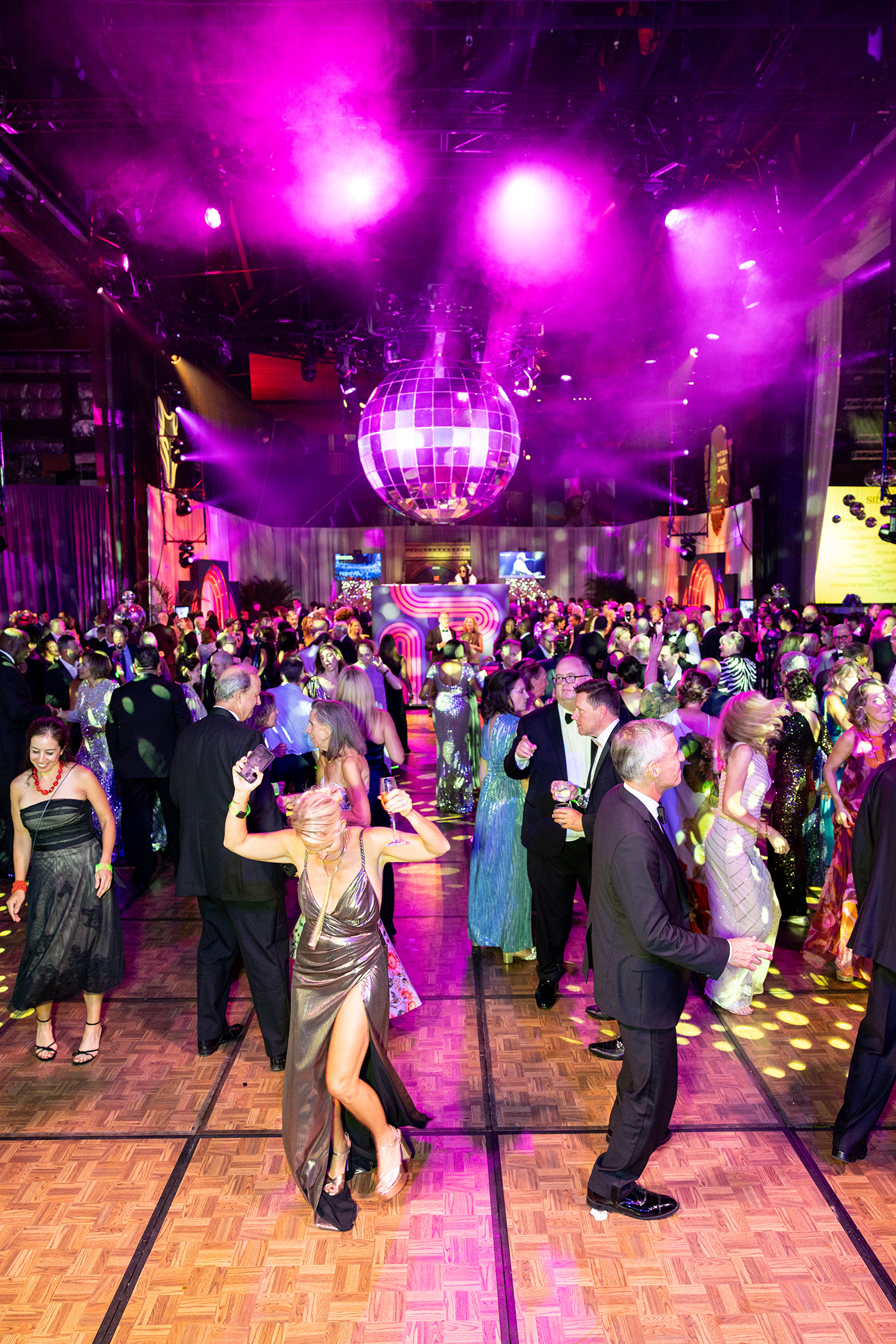 Ball guests dance joyfully under a dazzling giant disco ball.