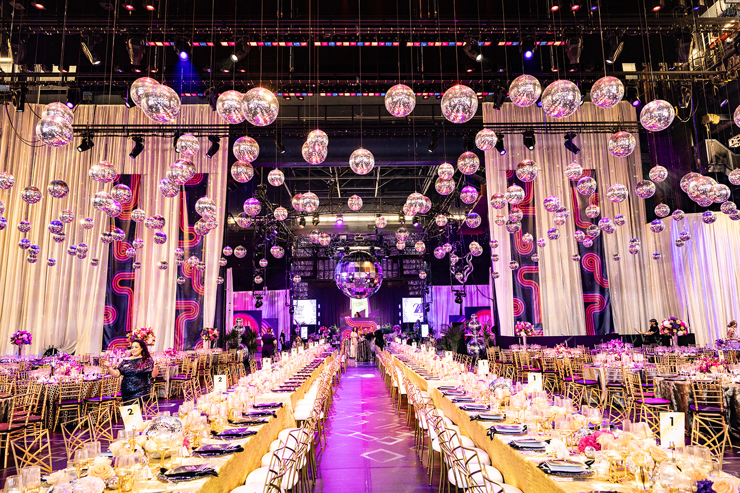 Long tables set up for a formal dinner, with hundreds of disco balls above.