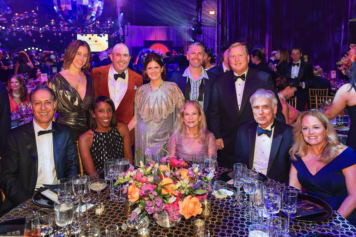 Friends dressed in disco-inspired formal attire pose around their table at the Wolf Trap Ball.