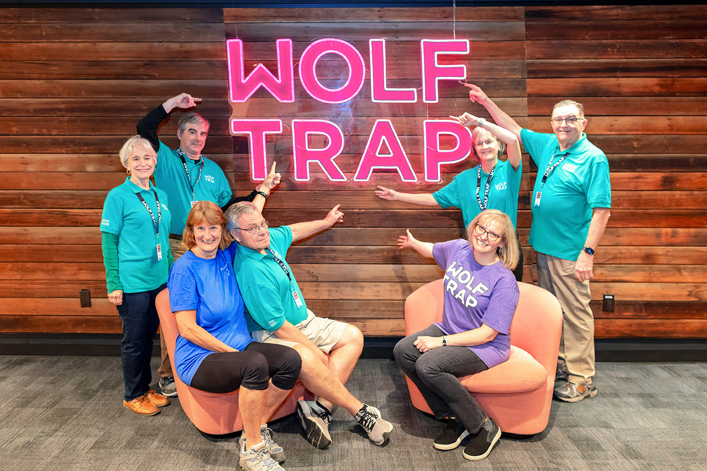 Wolf Trap Volunteers wearing teal shirts pose around a neon Wolf Trap sign.