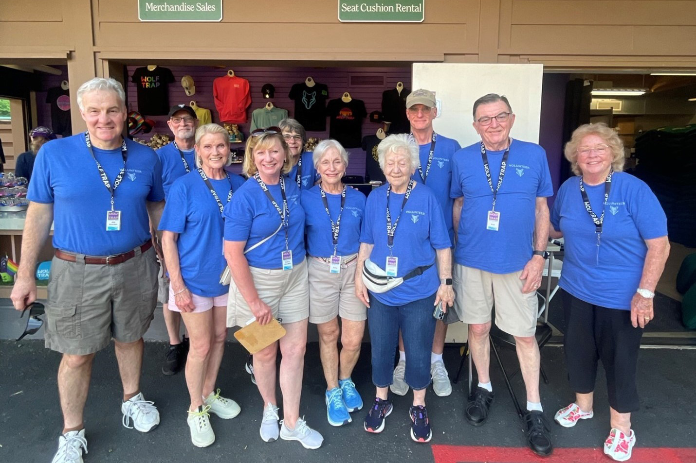 Big group of gift shop volunteers in blue shirts smile.