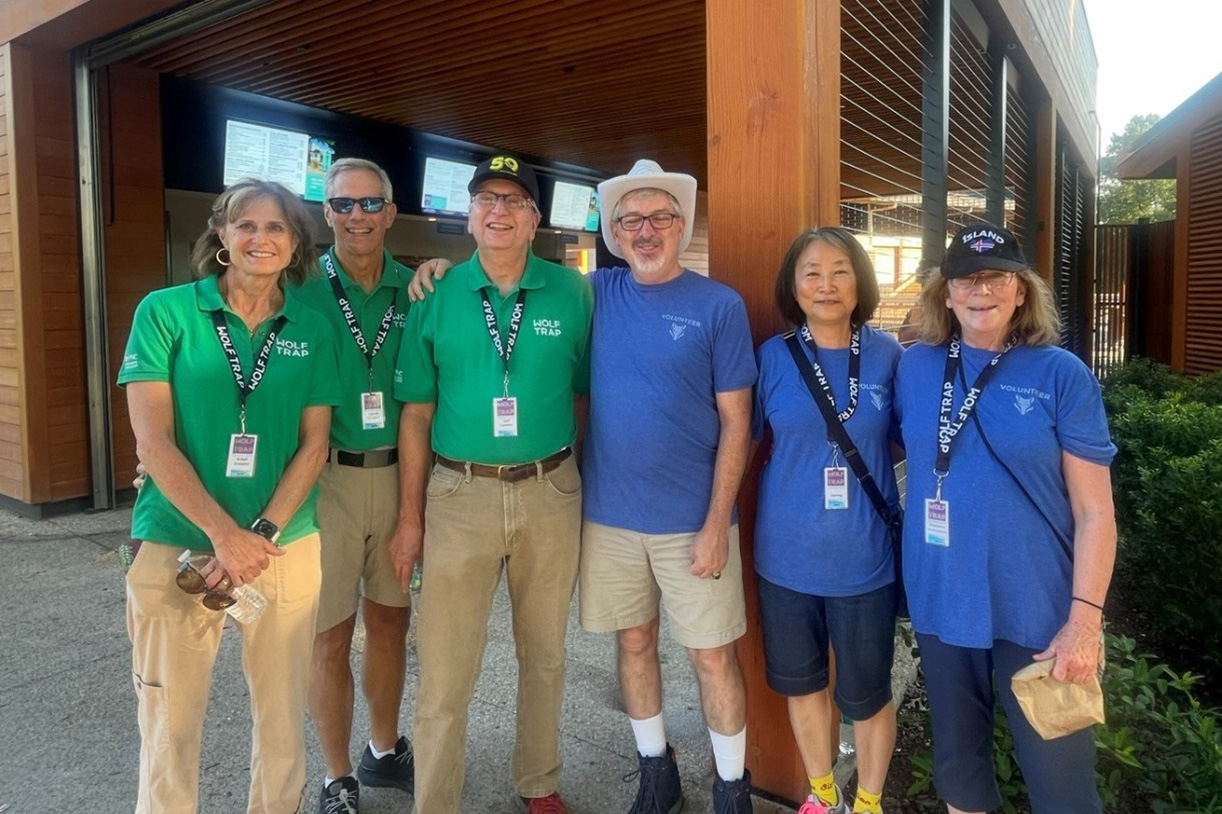 Volunteers in blue and green shirts pose in front of the Meadow Gate.