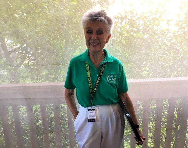 Wolf Trap Volunteer Bette Gorman poses at a railing overlooking Wolf Trap park on a sunny day.