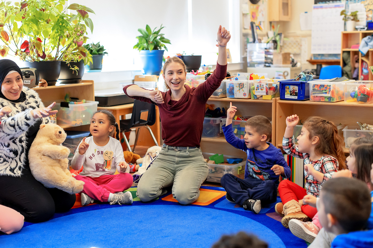 A Wolf Trap teaching artist leads an activity in the classroom, and children stretch their arms and smile.