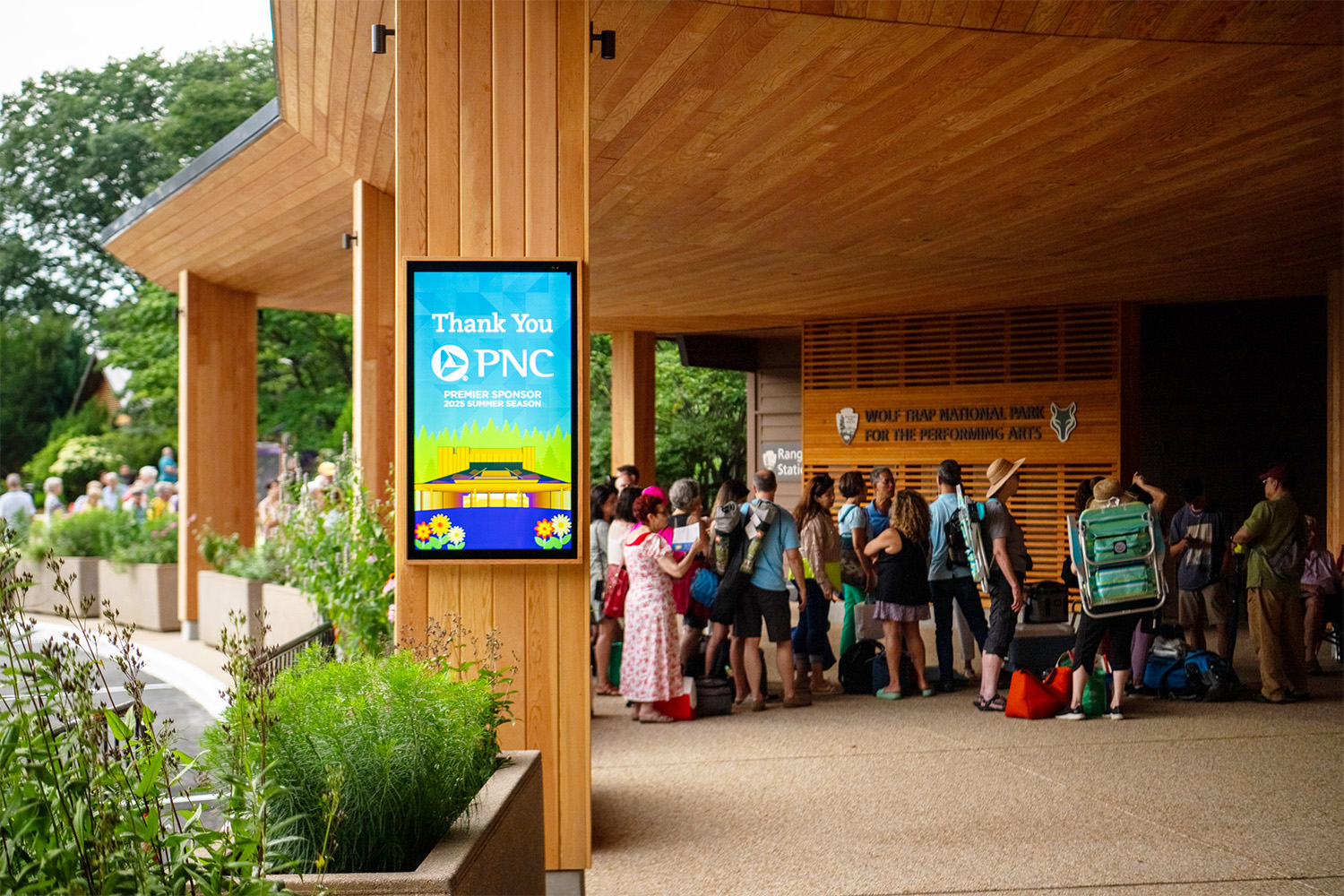 "Thank You, PNC" displayed on a screen outside of Wolf Trap's main gates, with patrons entering the park.