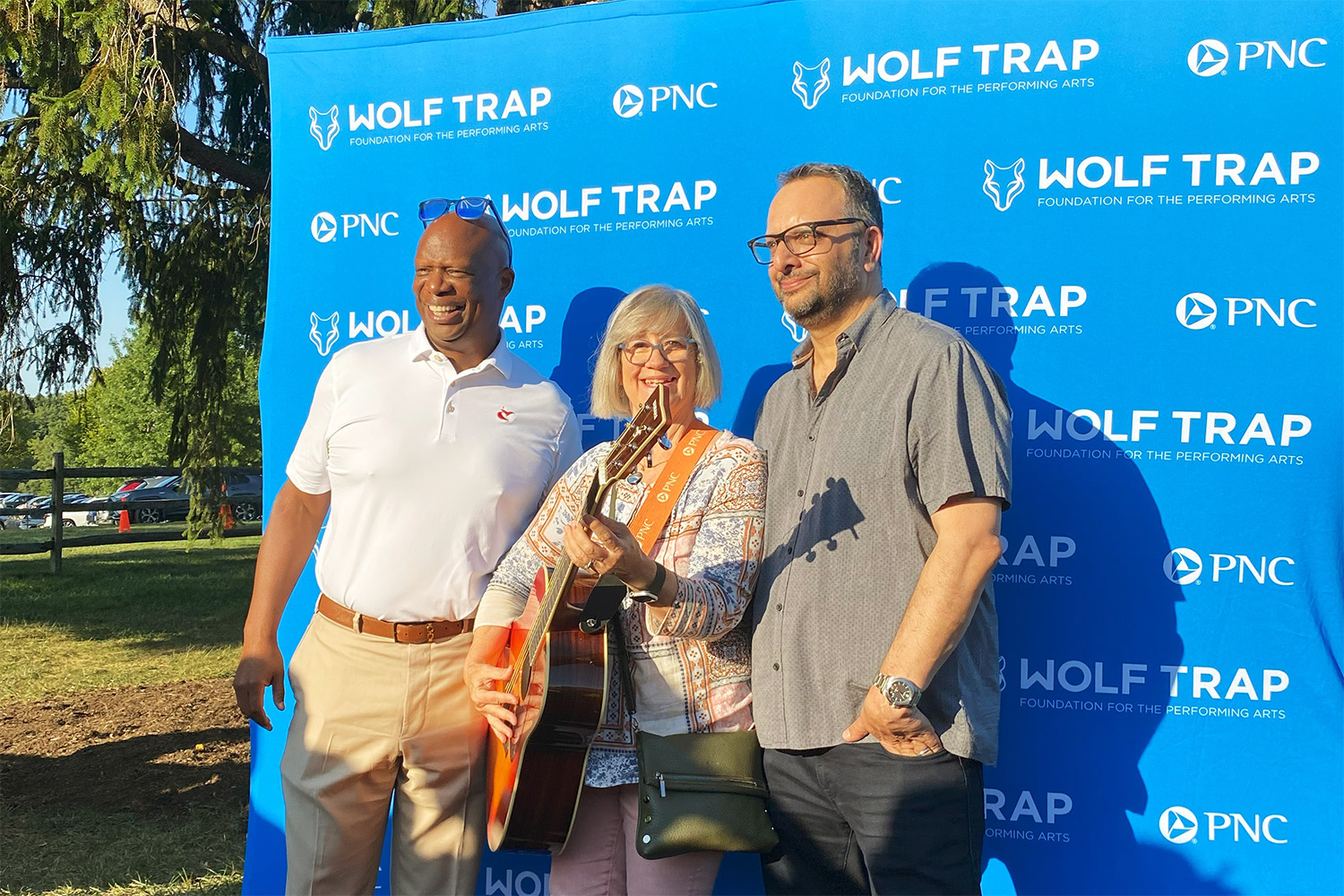 Arvind Manocha and Jermaine Johnson pose with the 2024 Rockstar for a Day contest winner, who is holding a guitar.