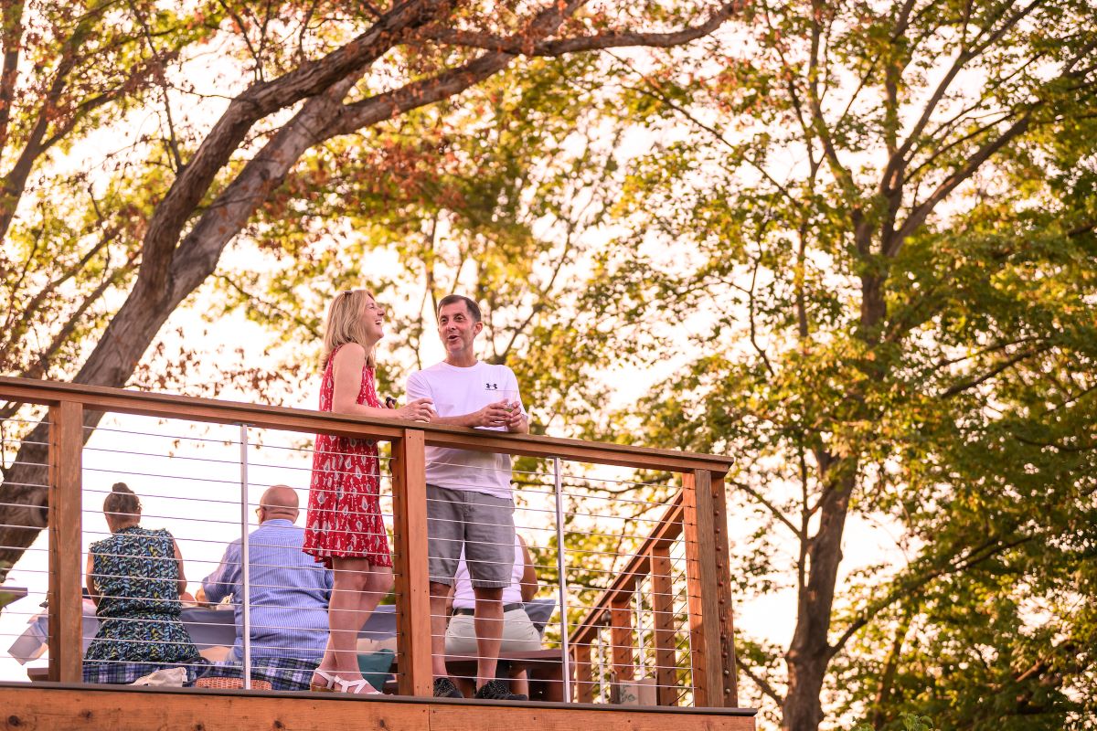 A woman and man stand at the railing of the Meadow Overlook picnic area and laugh together, with beautiful trees around them.