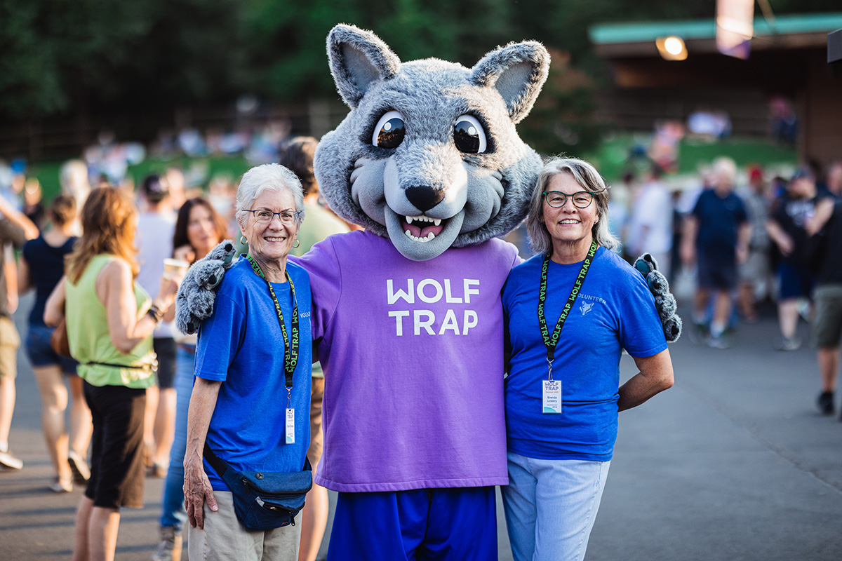 Wolf Trap volunteers pose with Wolfie, a cute wolf mascot in a purple shirt.