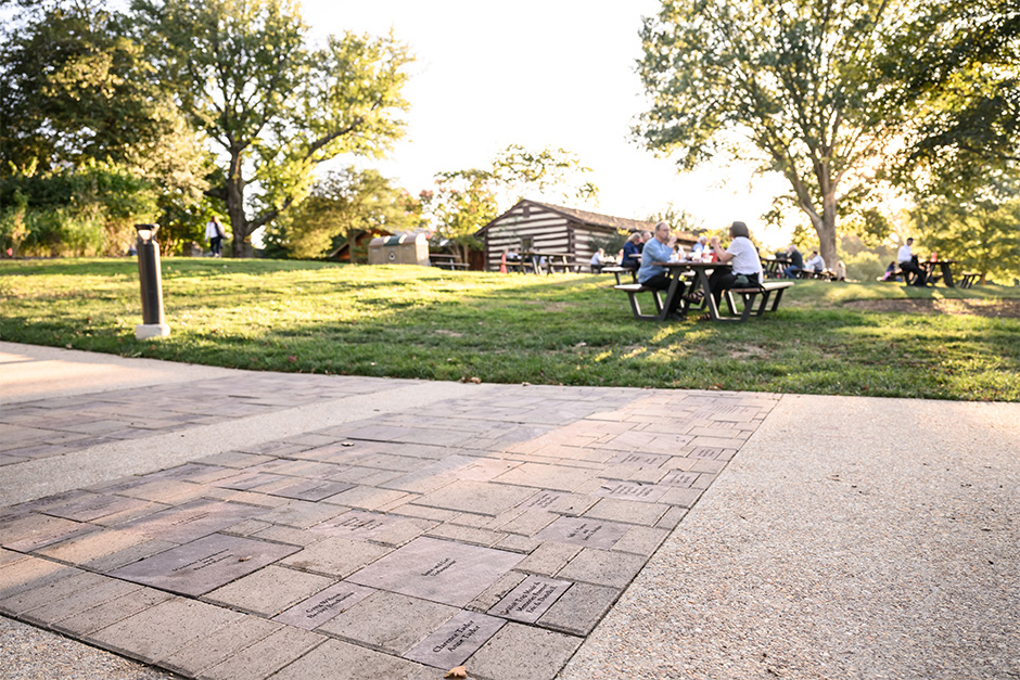 Closeup of the Pavers with a view of green trees and picnic tables with happy patrons.